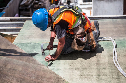 construction worker kneeling wearing blue hard hat and orange vest providing tpo flat roof installation service